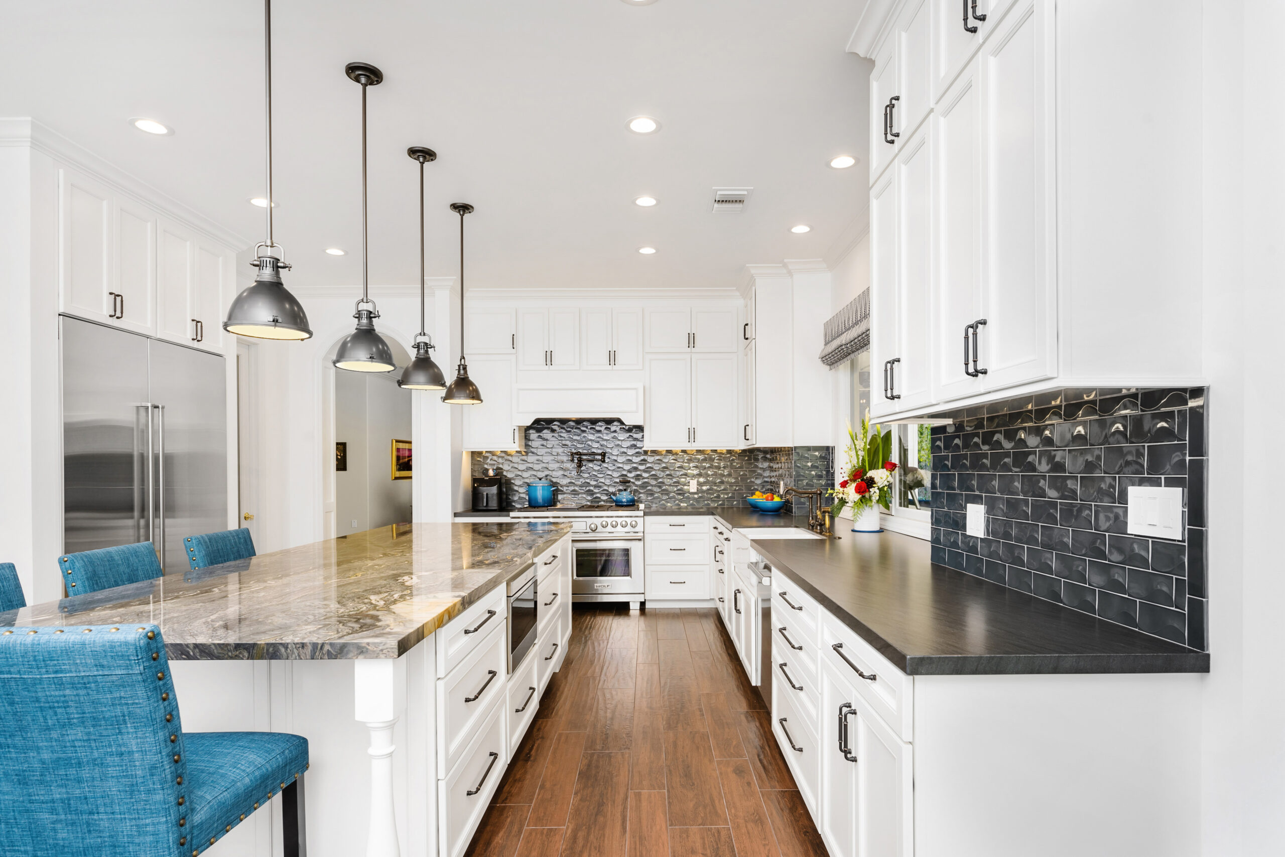 Bright kitchen with white cabinets, dark countertops, and hanging pendant lights